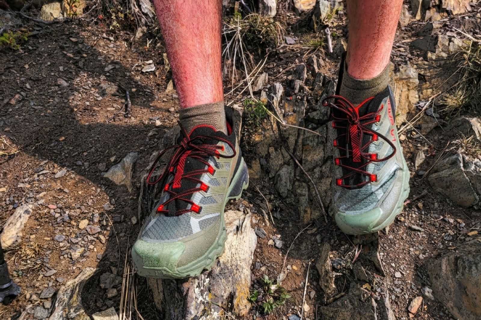 Close-up of hiking shoes with red laces on rocky terrain.