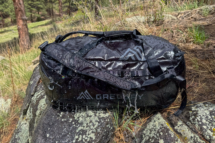 Black Gregory Alpaca 60 duffel covered in water droplets on rocks during weather-resistance testing.