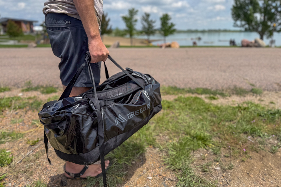 Person carrying the black Gregory Alpaca 60 duffel by the top handles near a lake.