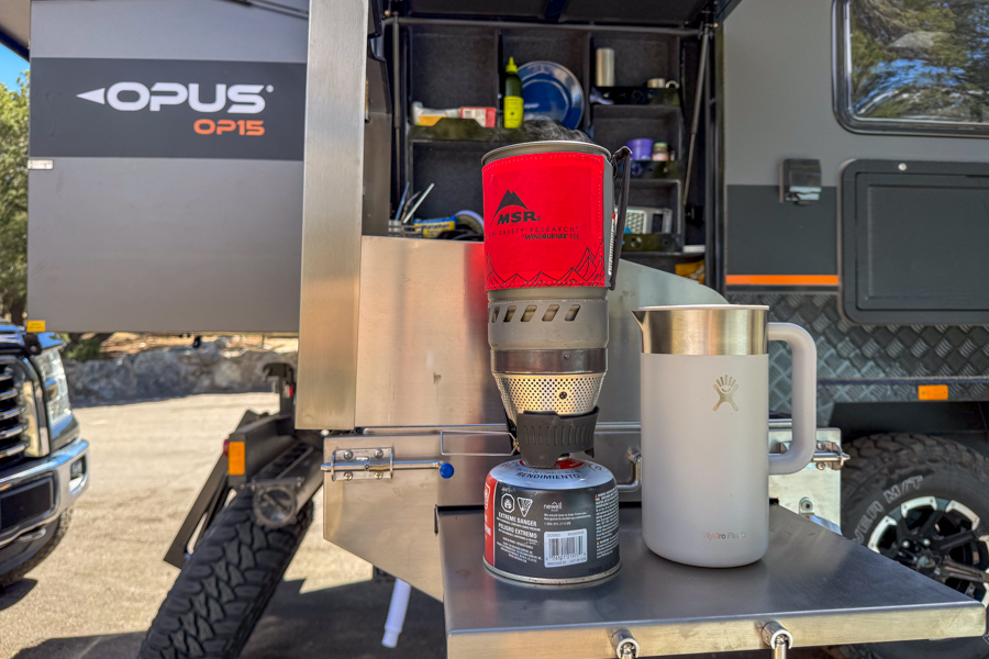 A French press sitting beside a camp stove setup on a trailer kitchen counter.