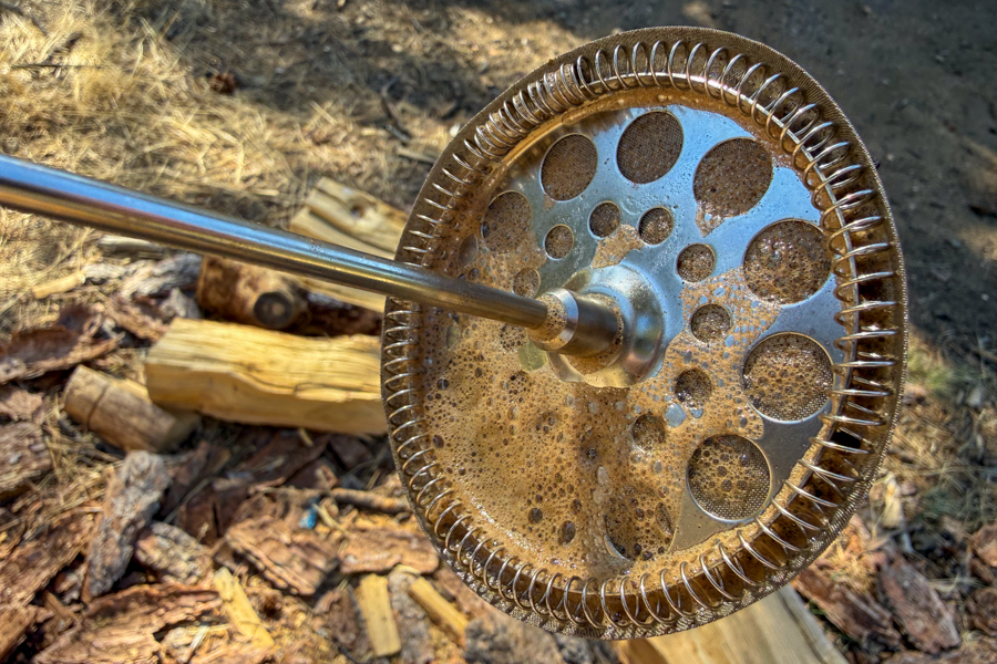 Close-up of a French press metal filter screen coated with coffee residue after brewing.