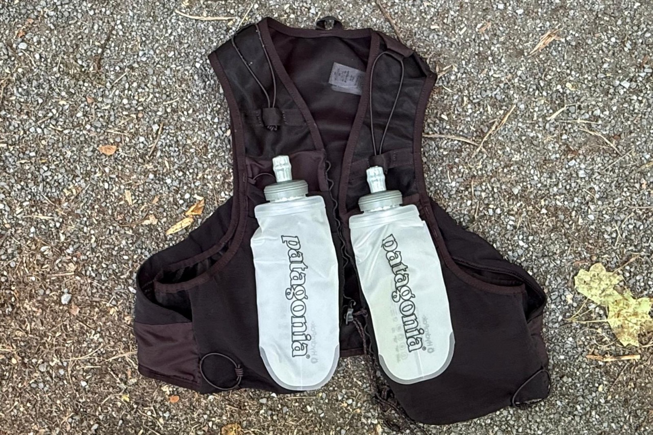 A black running vest lying on the ground with two water flasks on top of it.