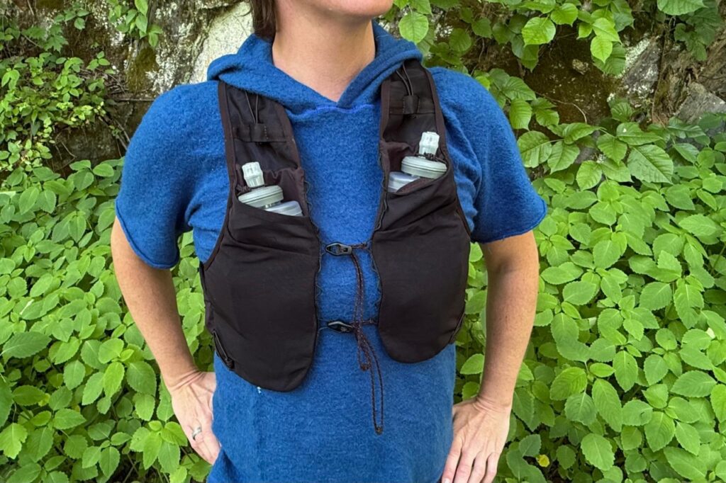 Close-up of a woman wearing a black running vest standing in front of greenery.