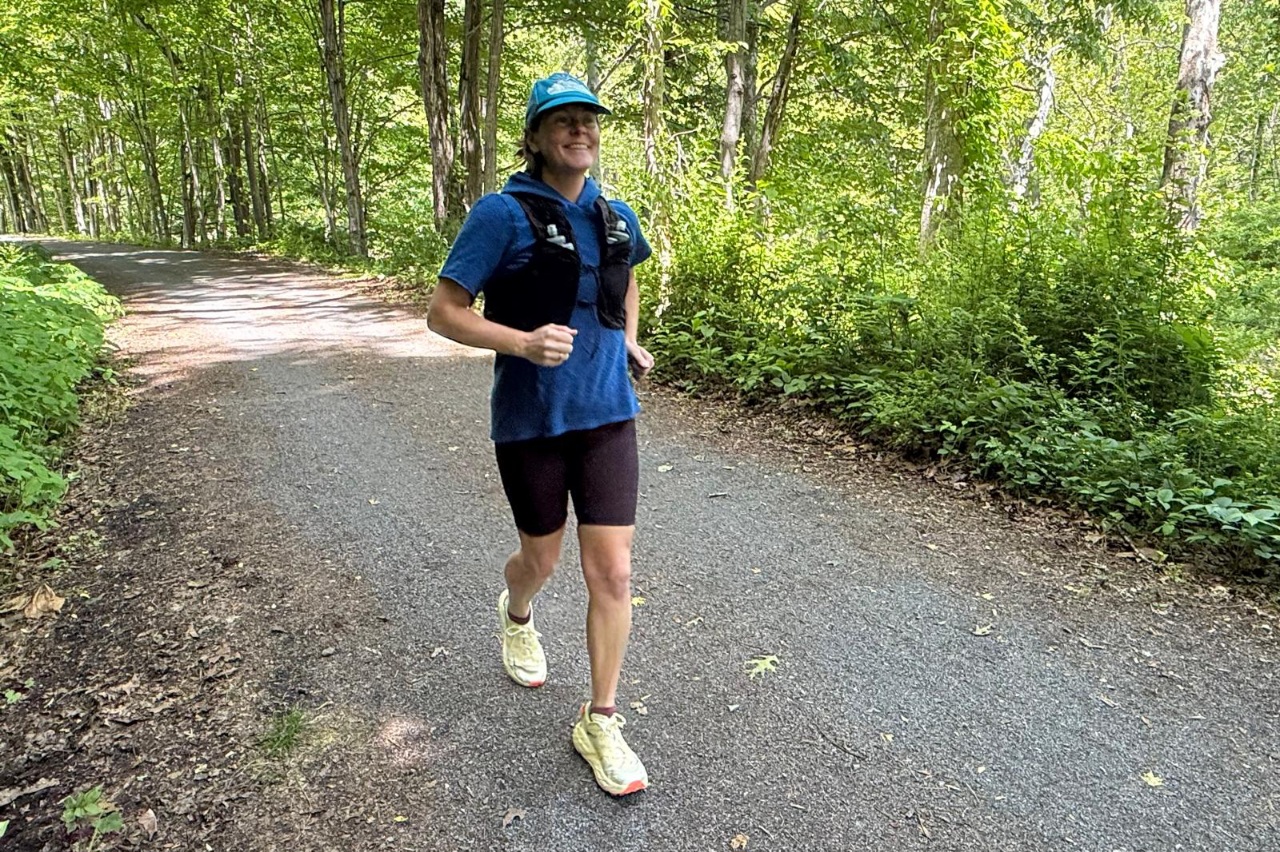 Woman wearing a black running vest while running on a flat, forested trail.