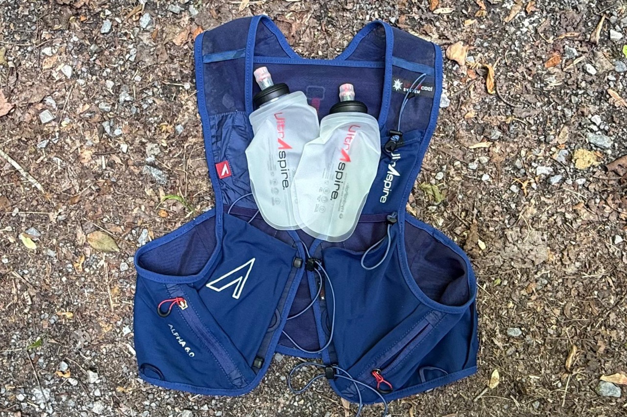 Close-up image of a blue running vest lying on the ground with two empty water flasks lying on top of it.