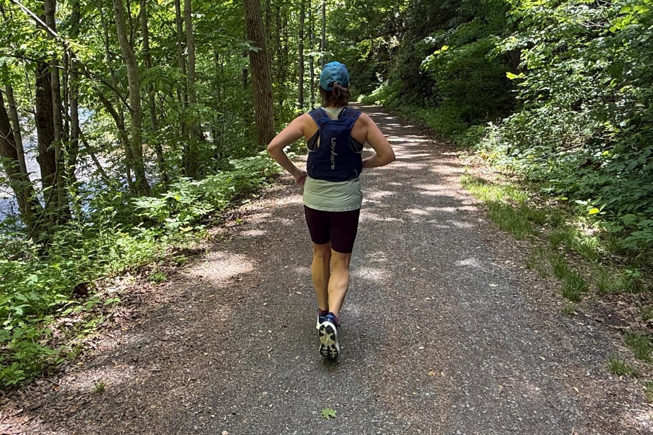 Runner wearing a hydration vest while running on a forested, flat trail.