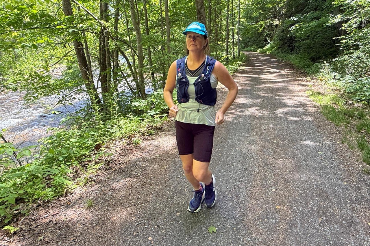 Runner wearing a hydration vest on a forested, flat trail.
