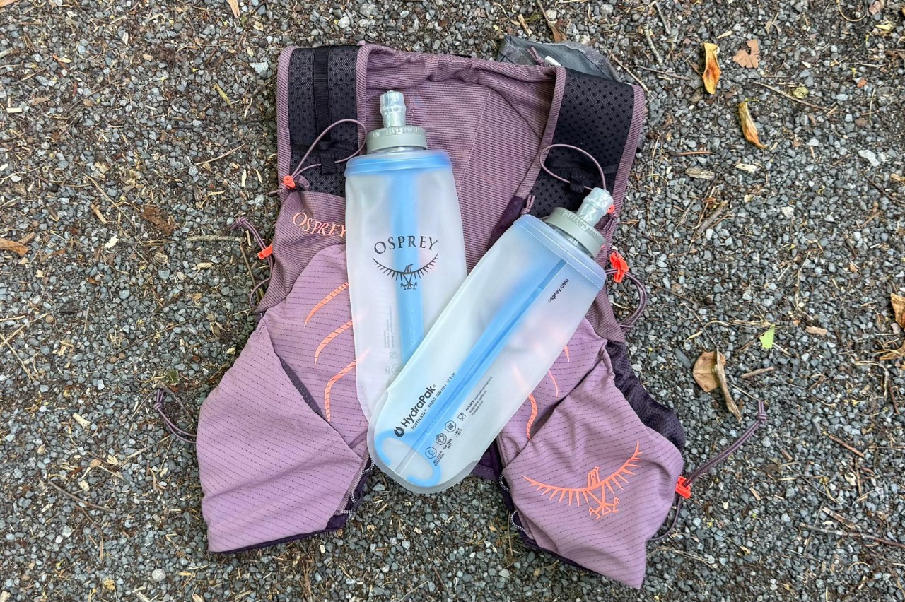 A purple running vest lies on the ground with two water flasks on top of it.