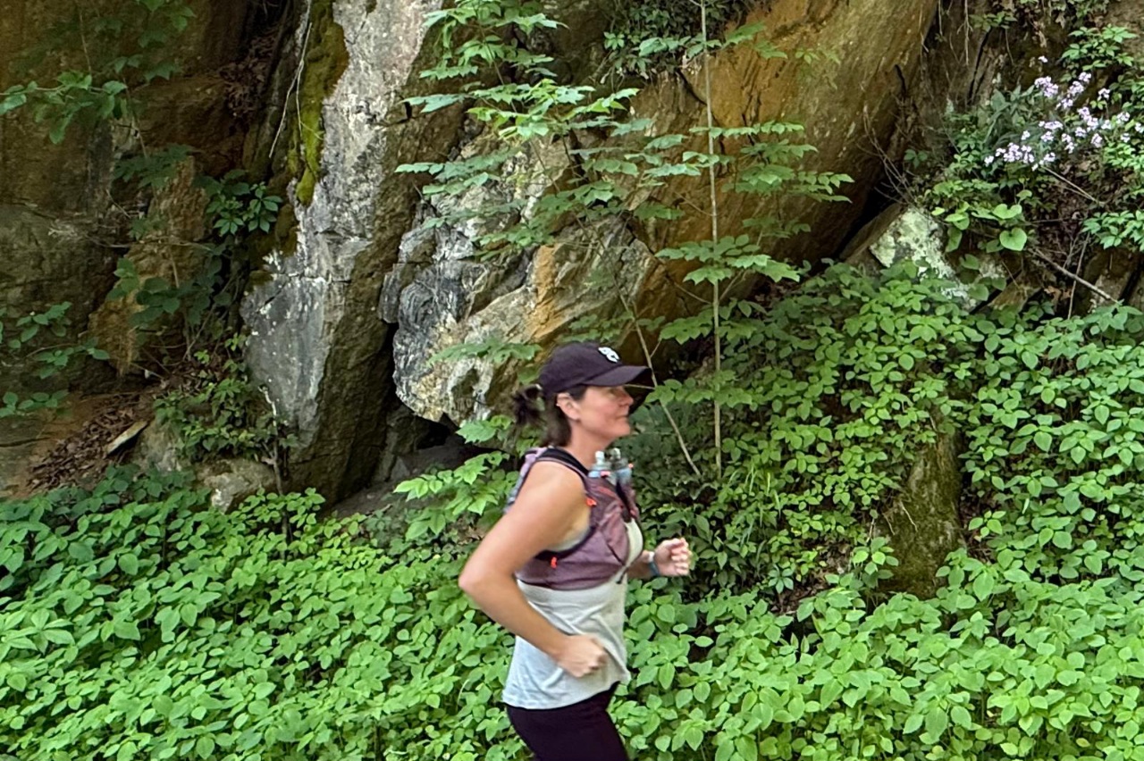 Woman wearing a purple hydration vest while running with greenery in the background.