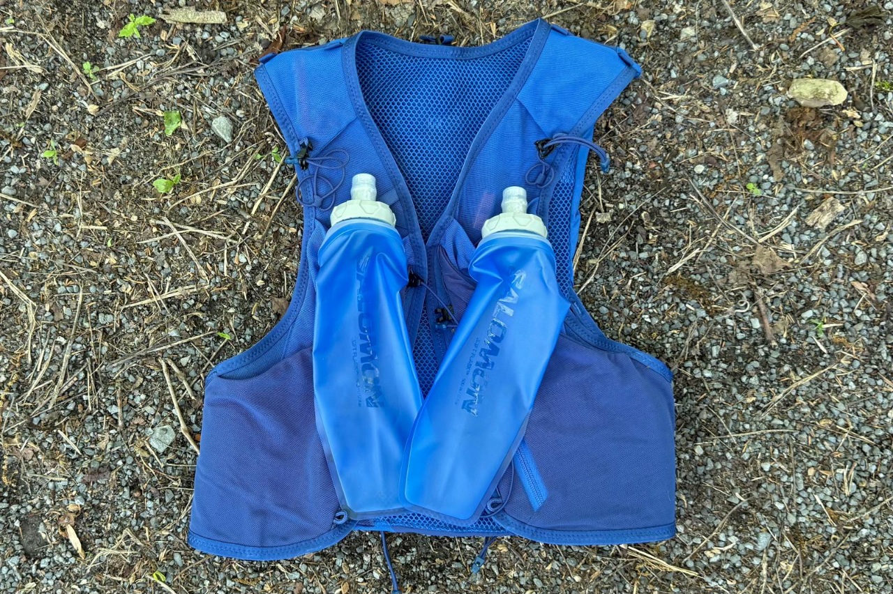 A blue running vest lying on the ground with two water flasks on top of it.