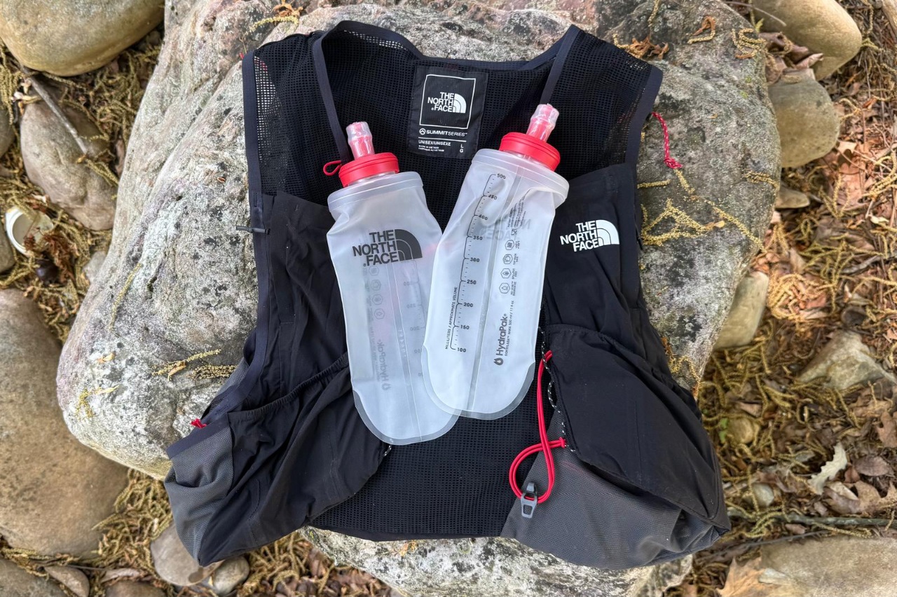 A black running vest lying on the ground with two empty water flasks on top of it.