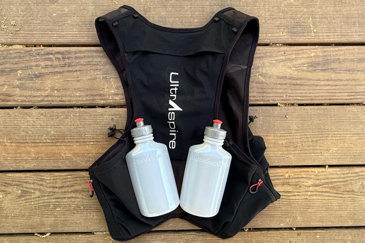 Close-up image of a black running vest laid on a picnic table with two water bottles on top of it.