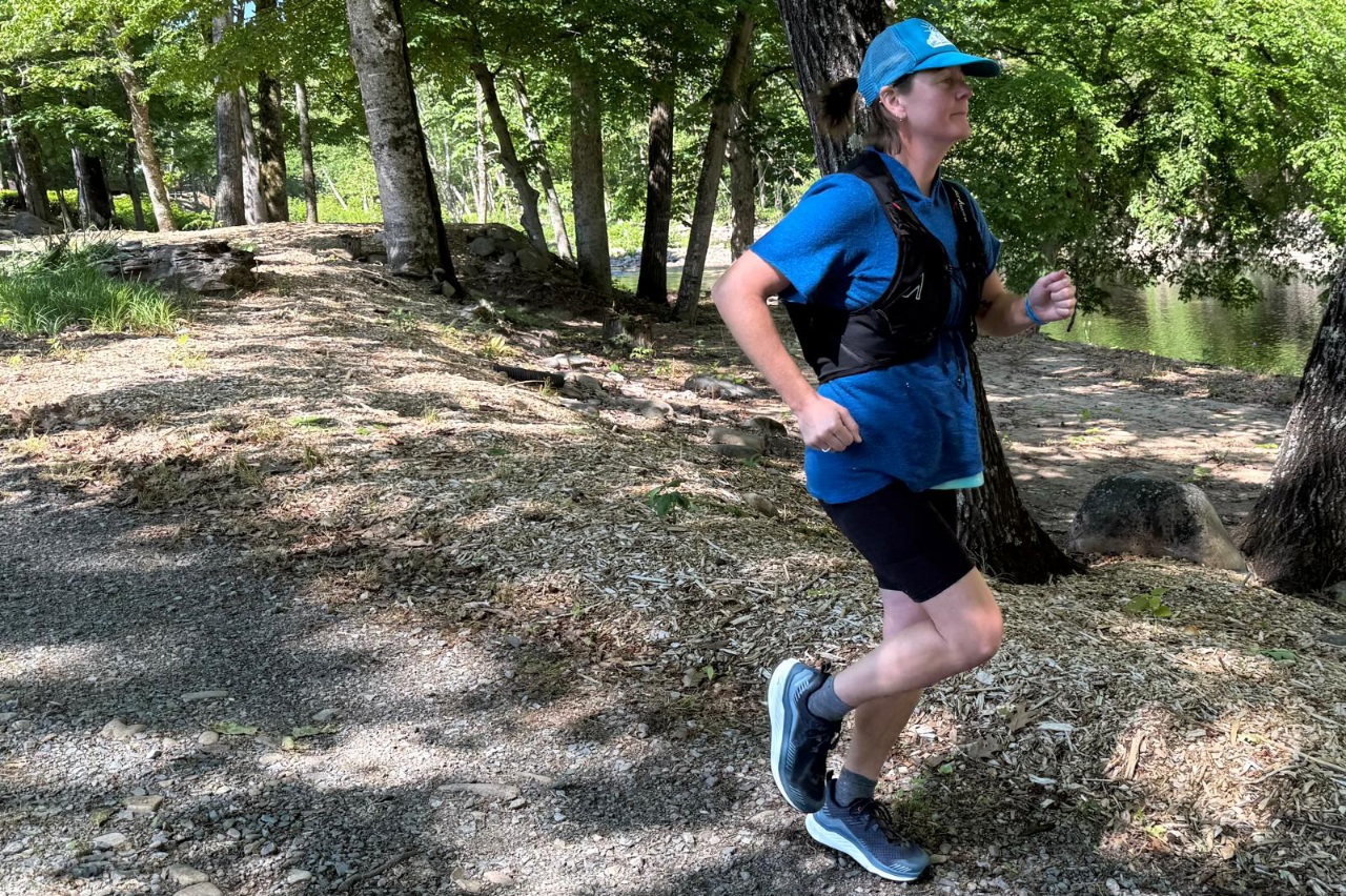Woman running on a forested trail wearing a black running vest.