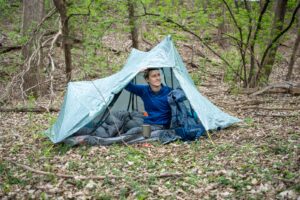 a man in blue sits in a tent in the forest
