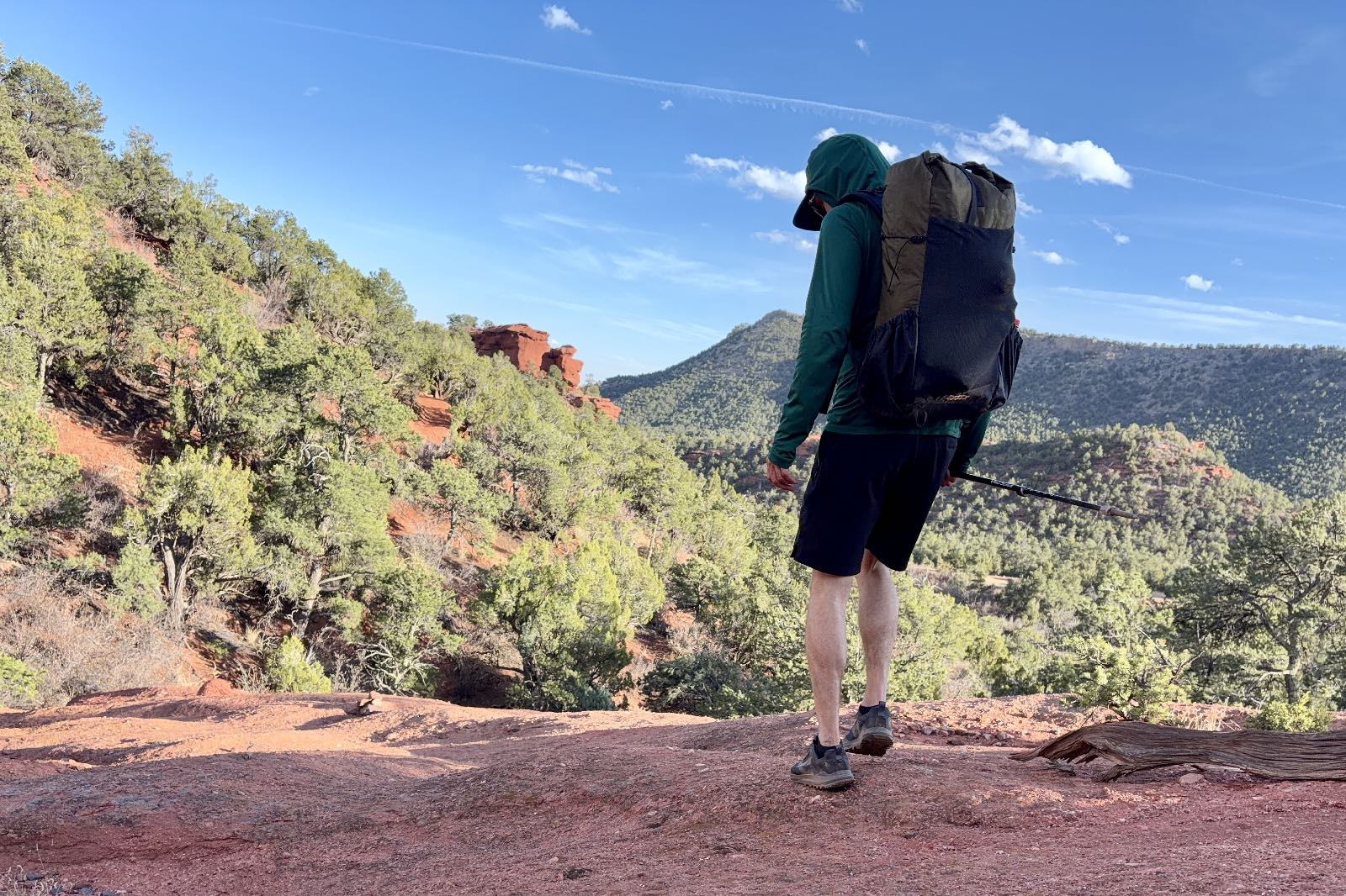 A hiker wearing a green backpack steps down a red rock trail.