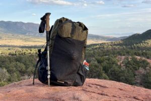 A green backpack with a trekking pole attached sits on red sandstone.