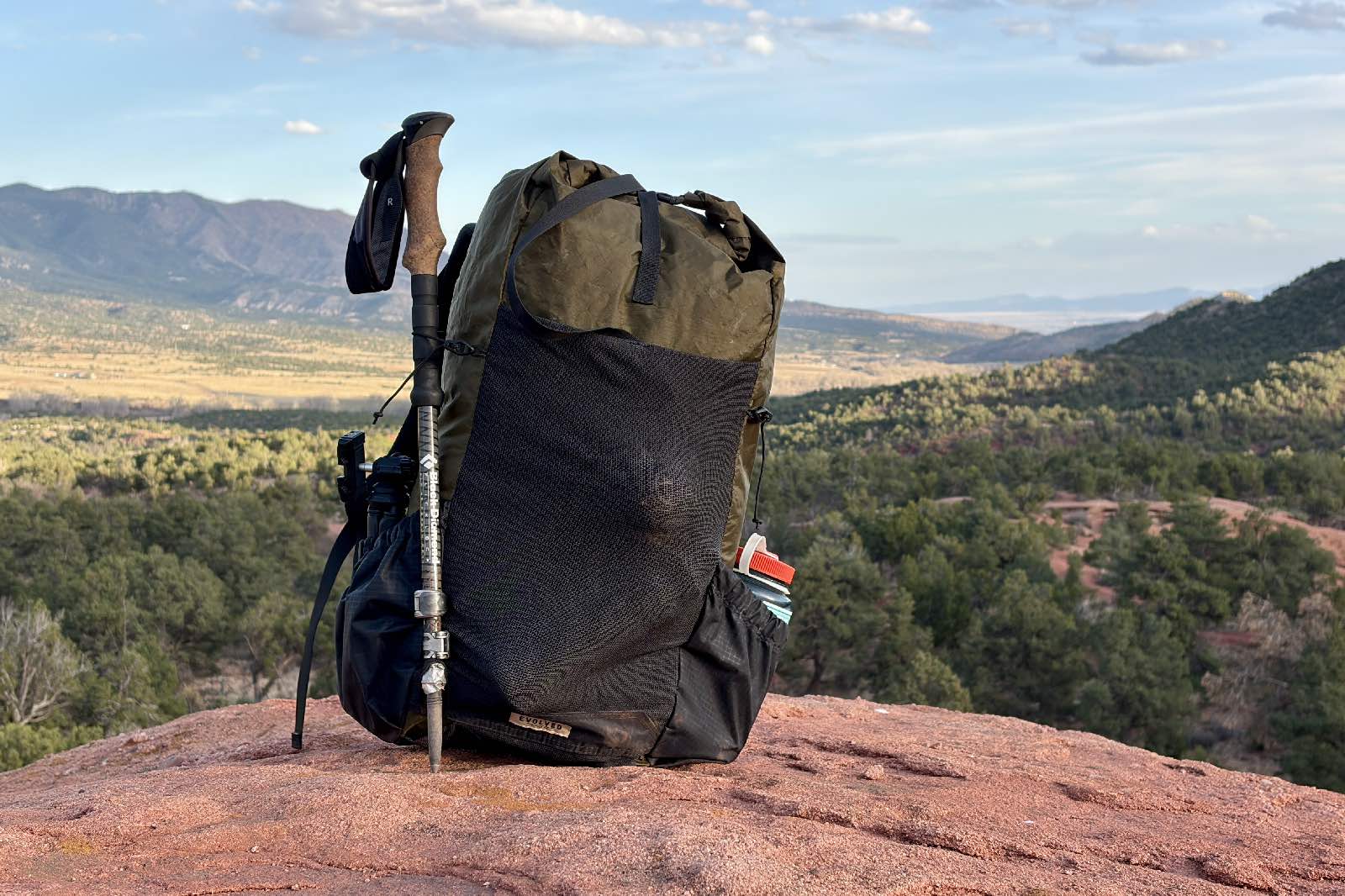 A green backpack with a trekking pole attached sits on red sandstone.