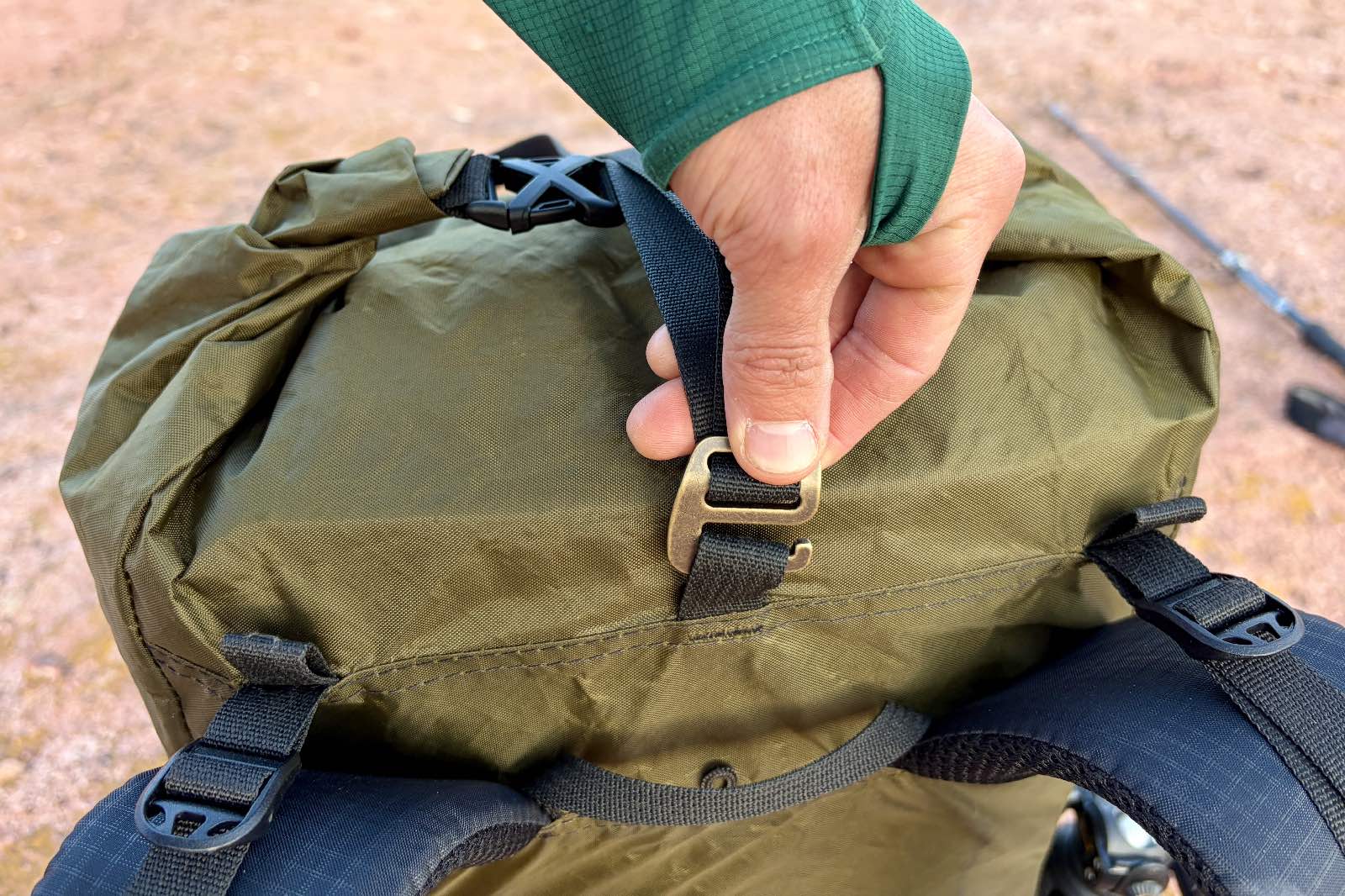 A close up of a hand holding a G-clip on a green backpack.