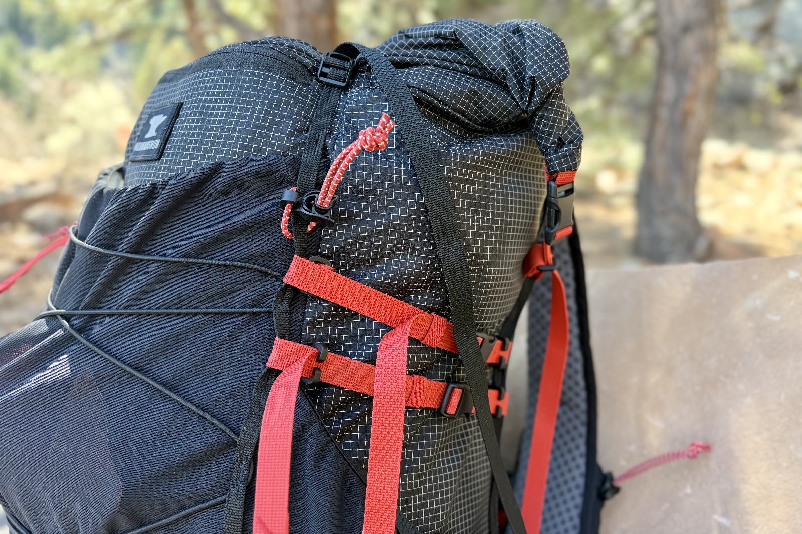 A close up of the top half of a black ultralight pack with red straps.