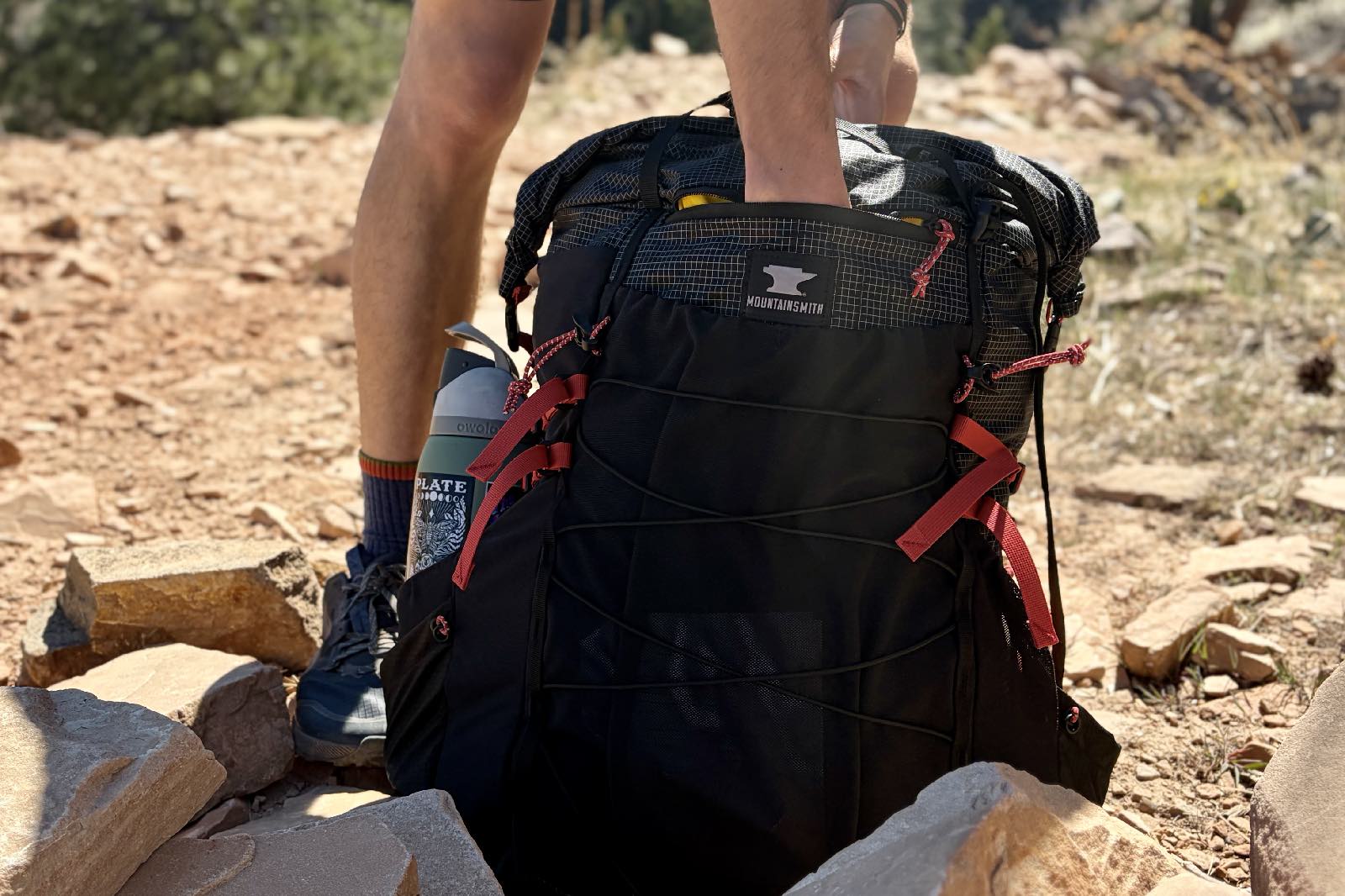 A hiker reaches into the outside zipper pocket of an ultralight backpack.