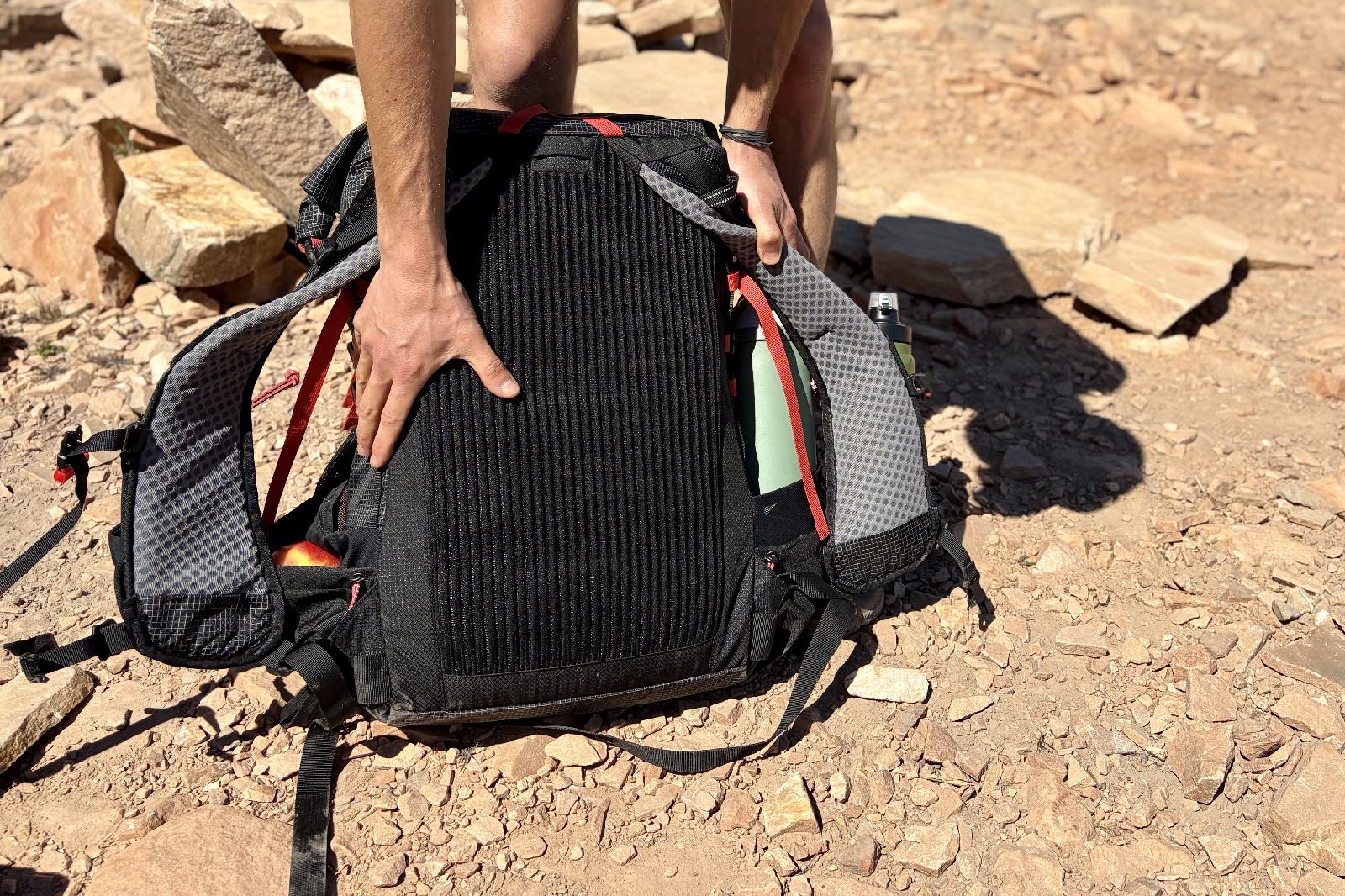 A hand feels the back panel of a black backpack.