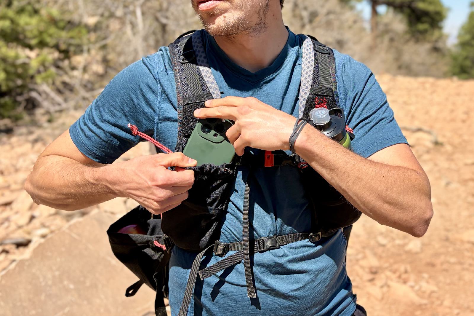 A hiker slides his smartphone into the shoulder strap pocket of his backpack.