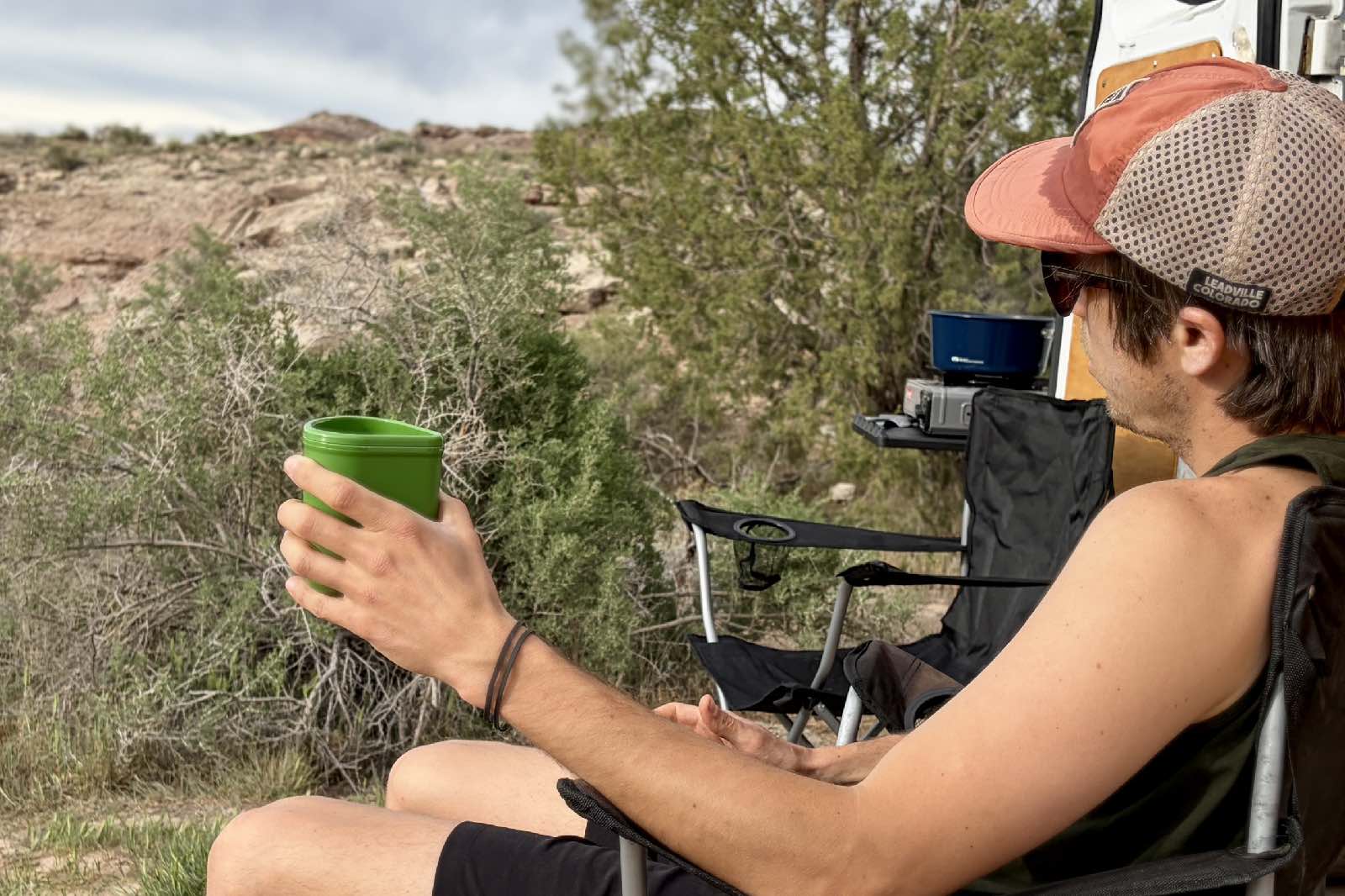 a person relaxing in a camp chair with a green cup in his hand