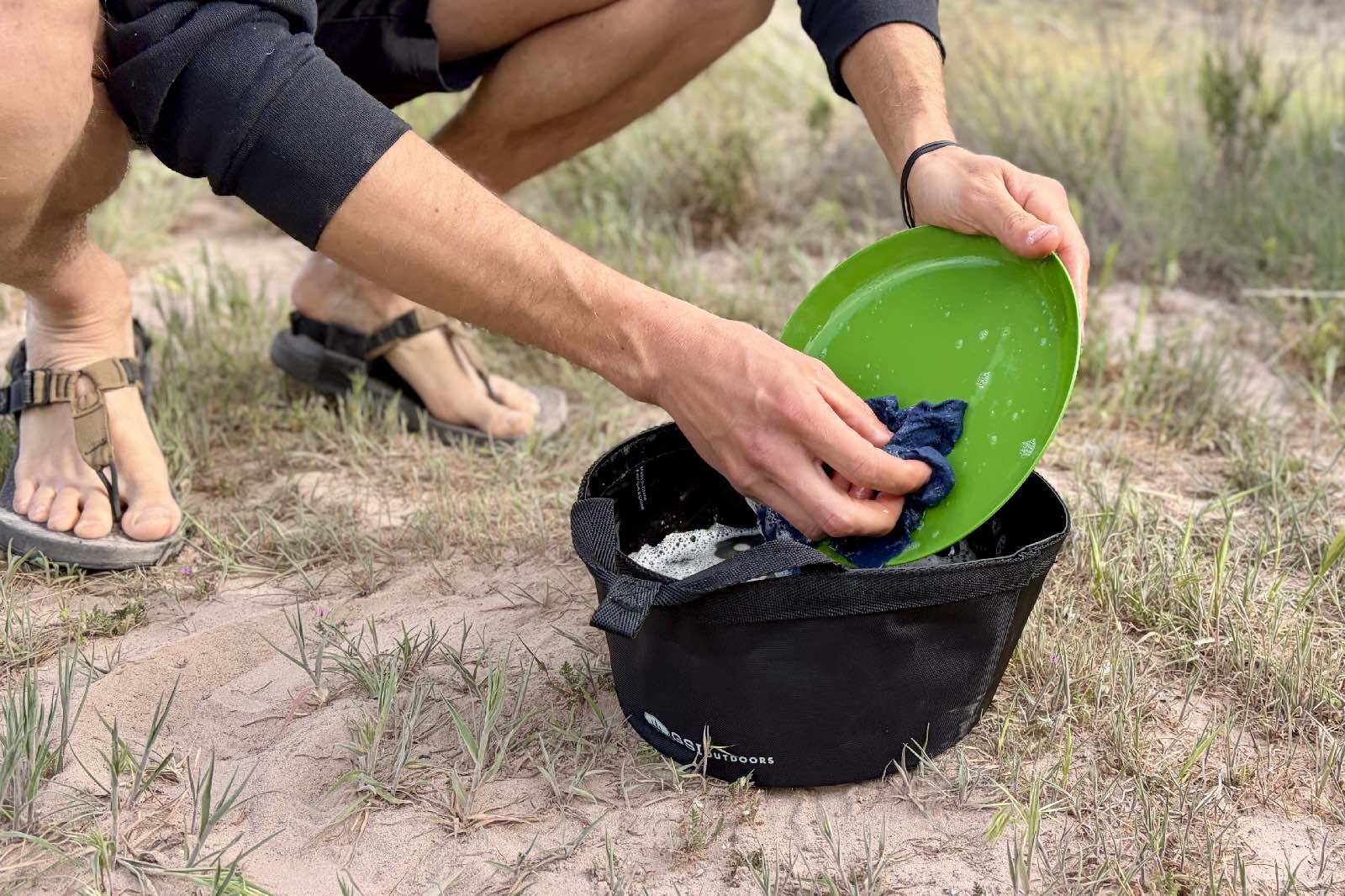 a close up of a hiker crouching down to do dishes in a wash basin