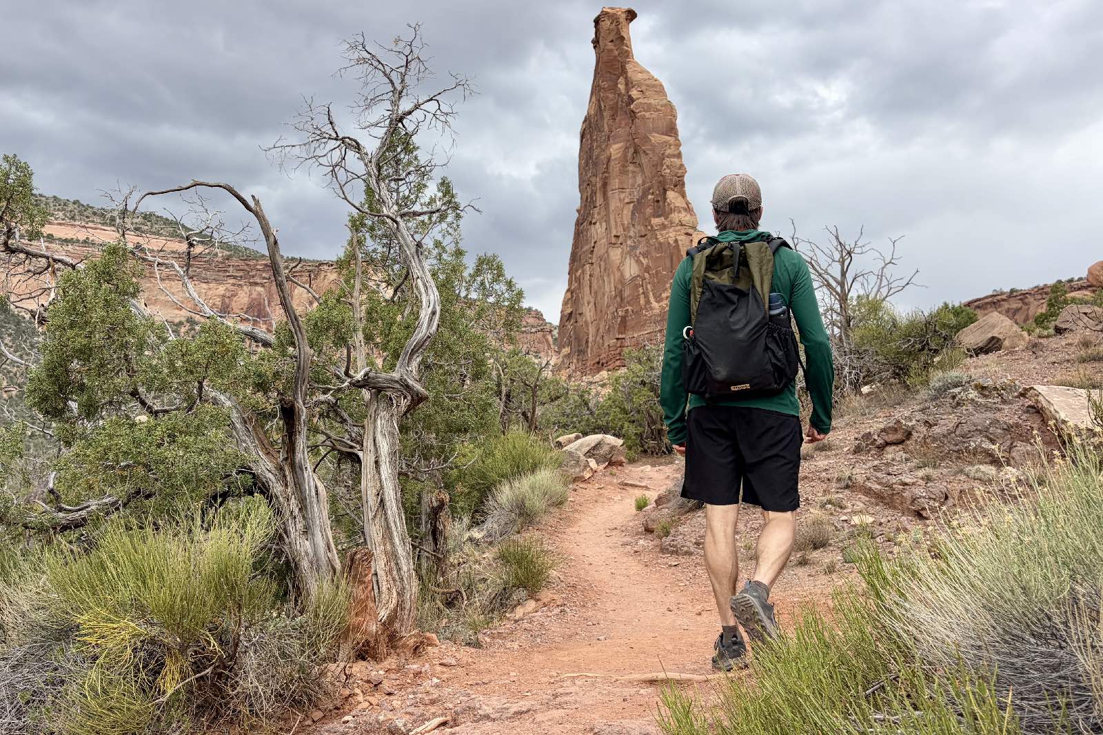 A hiker hikes through a red rock desert wearing a green backpack.