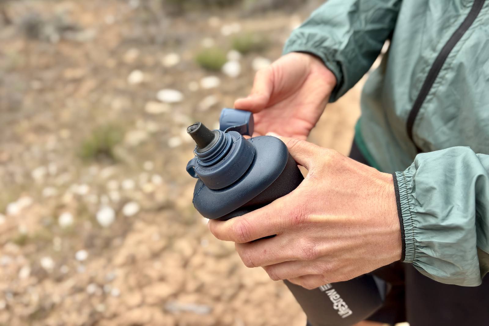 Close-up image of a hiker pulling the cap off of a soft flask water bottle.