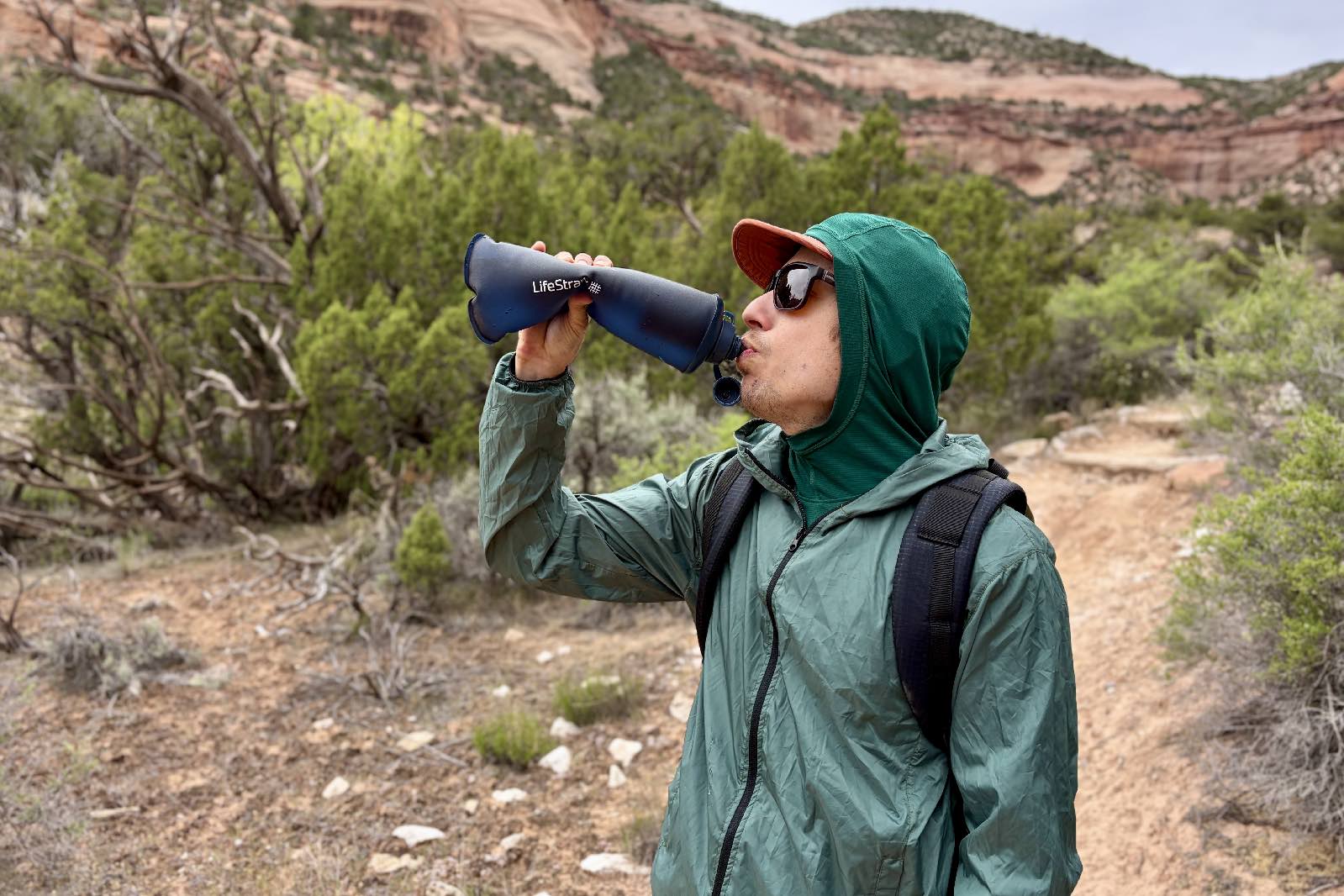 a hiker drinks from a soft flask water bottle in a desert setting