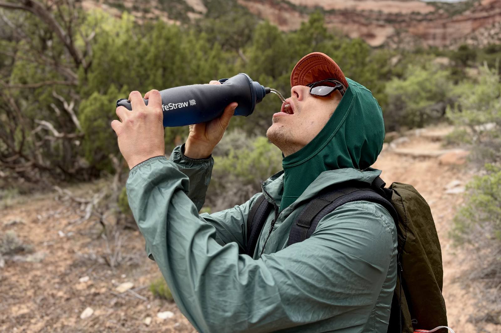 A hiker squirts water from a soft water bottler into his mouth.