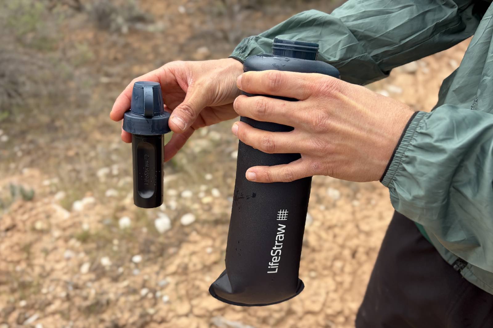 Close-up image of a hiker holding a soft water bottle and a water filter attachment.