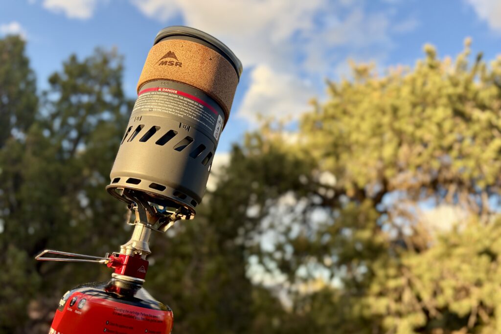 Close-up image of an MSR stove on top of a fuel canister with a view of trees and the sky above.