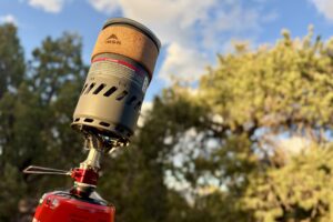 Close-up image of an MSR stove on top of a fuel canister with a view of trees and the sky above.