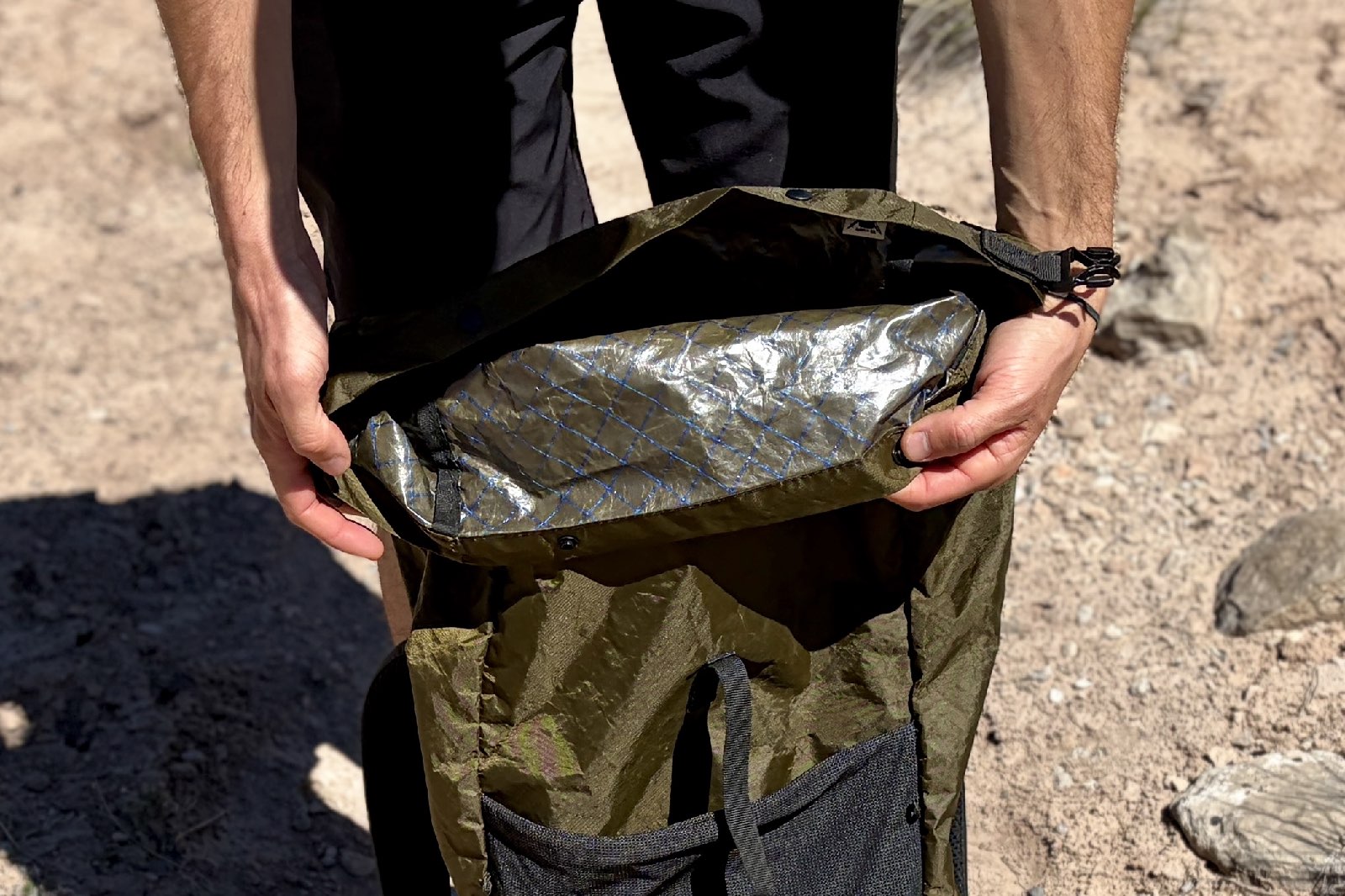 A close up of a hiker rolling down the top of a backpack with his hands.
