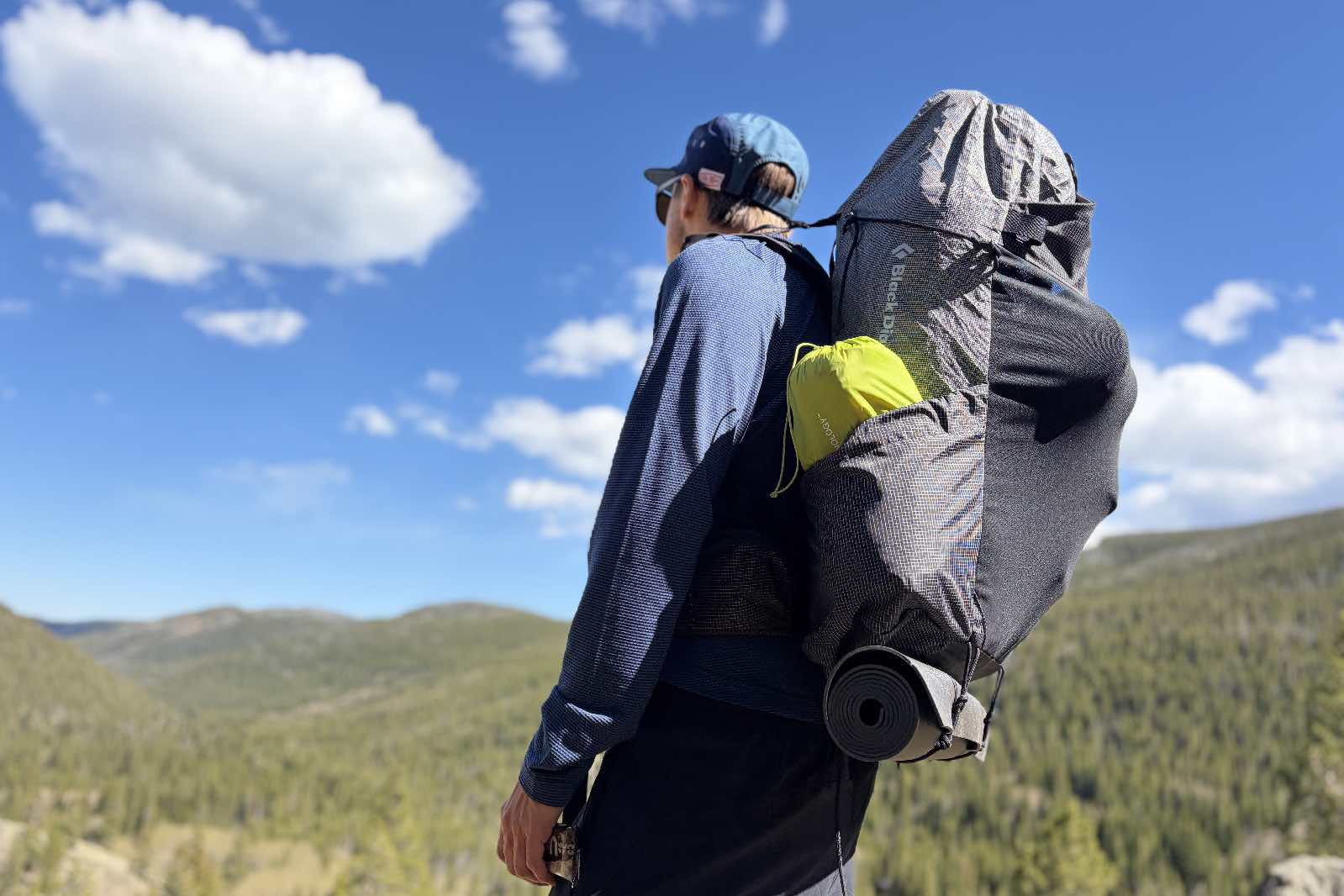 Un excursionista se encuentra frente a una vista de la montaña con una mochila gris.