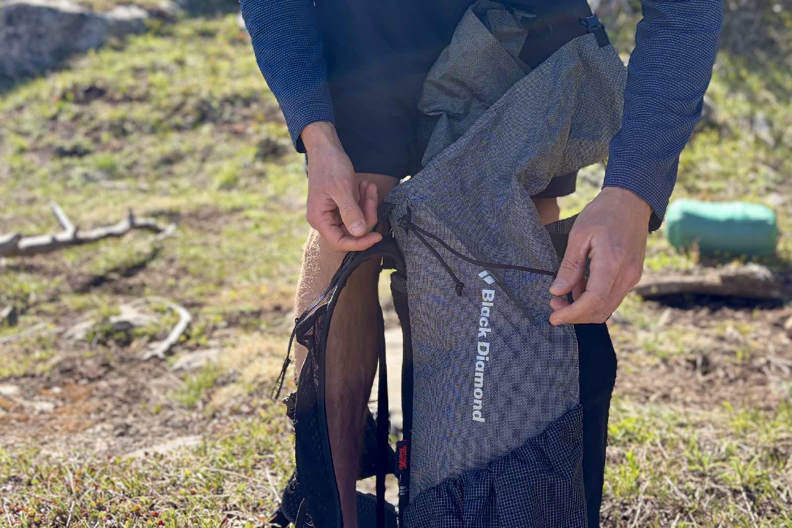 Primer plano de un excursionista agachado cerca de una mochila gris de diamantes negros.