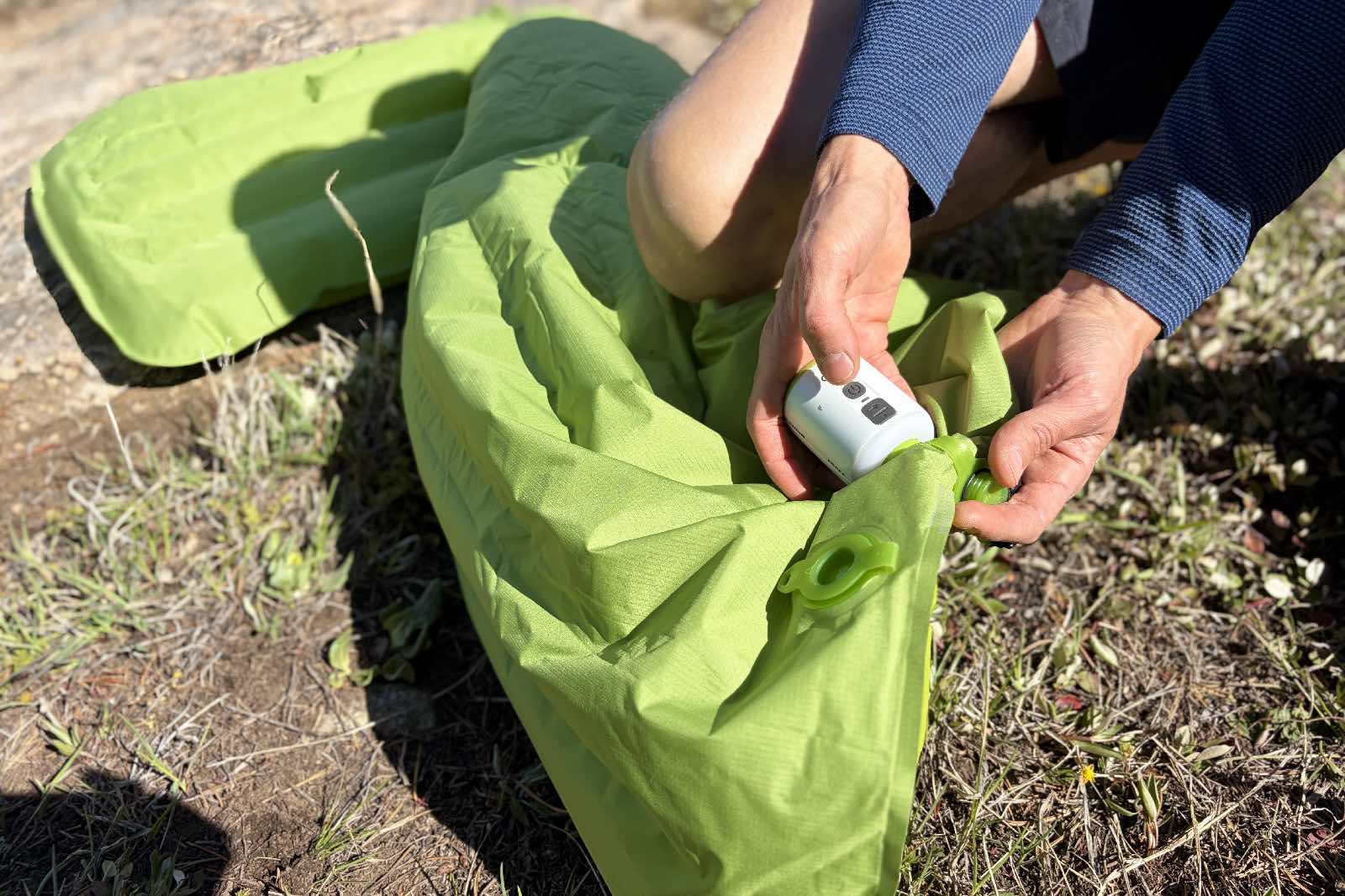 a hiker attaches an electric pump to a green inflatable sleeping pad