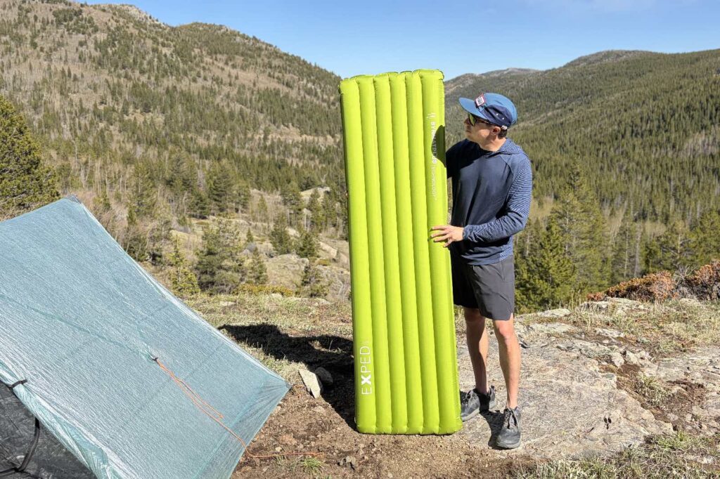 a hiker stands next to a green inflatable sleeping pad
