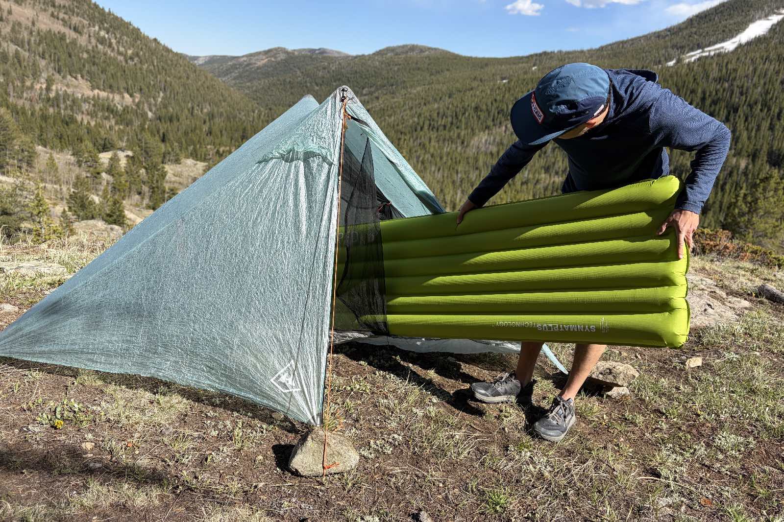 a hiker slides a green inflatable sleeping pad into a tent