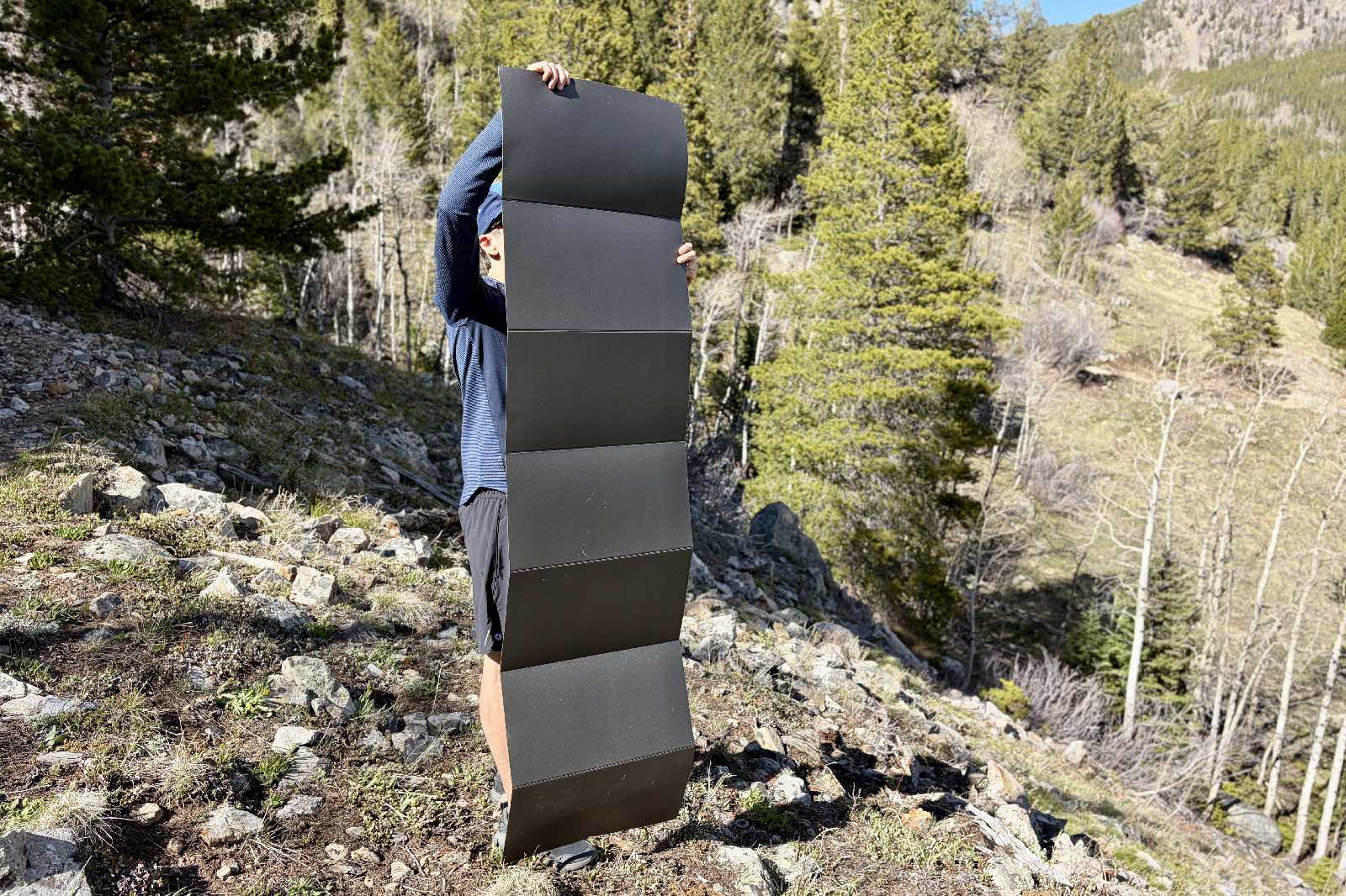 a hiker holds a foam sleeping pad fully unfolded