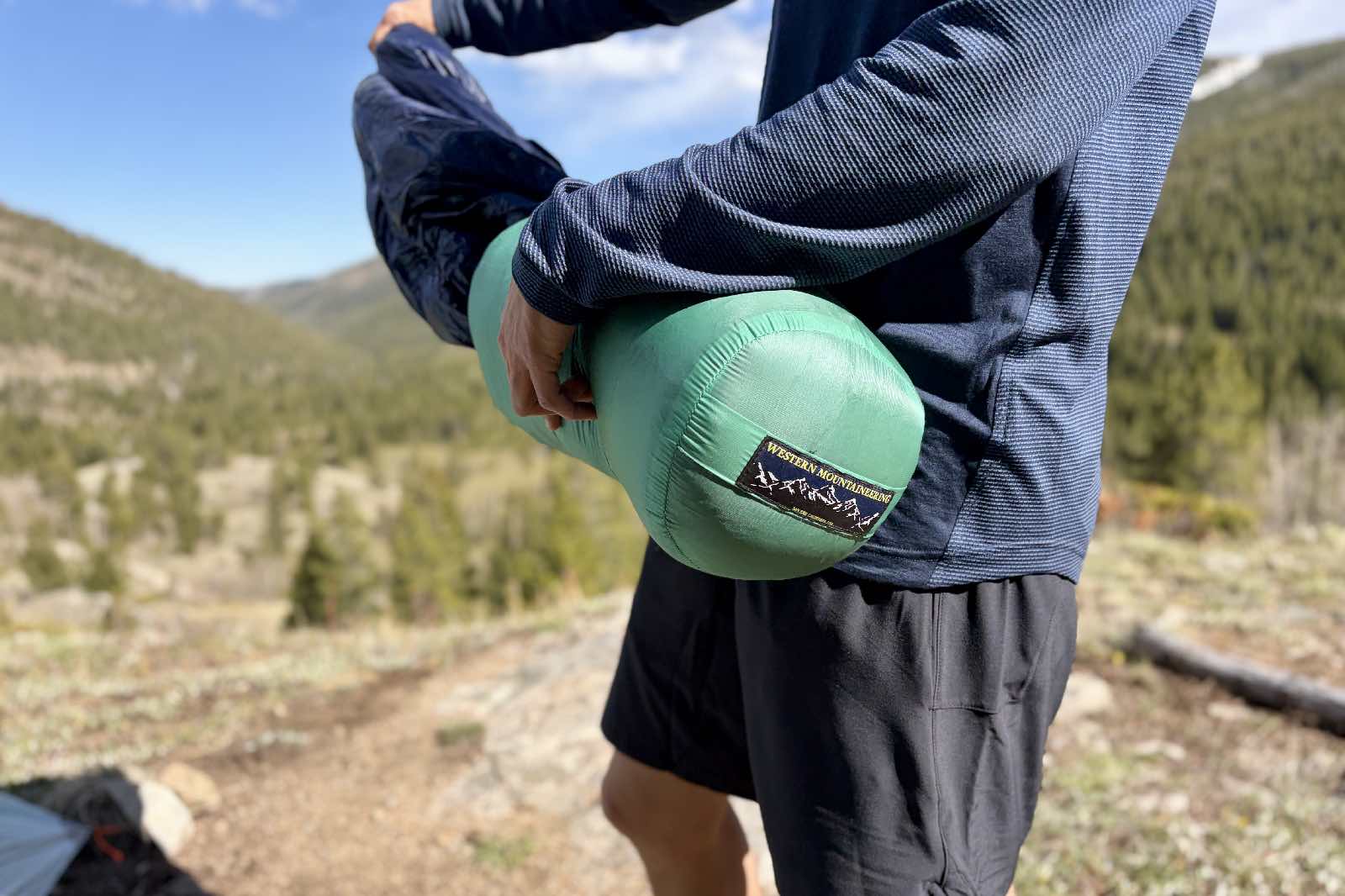 A hiker pulls a down sleeping bag out of its stuff sack
