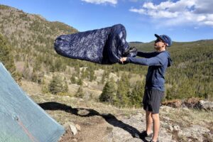 a hiker shakes out a blue sleeping bag