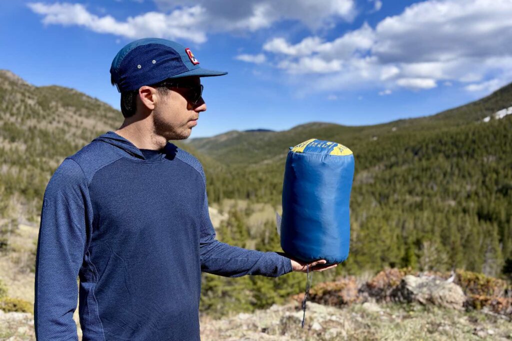 a hiker holds a blue sleeping back stuffed into a stuff sack