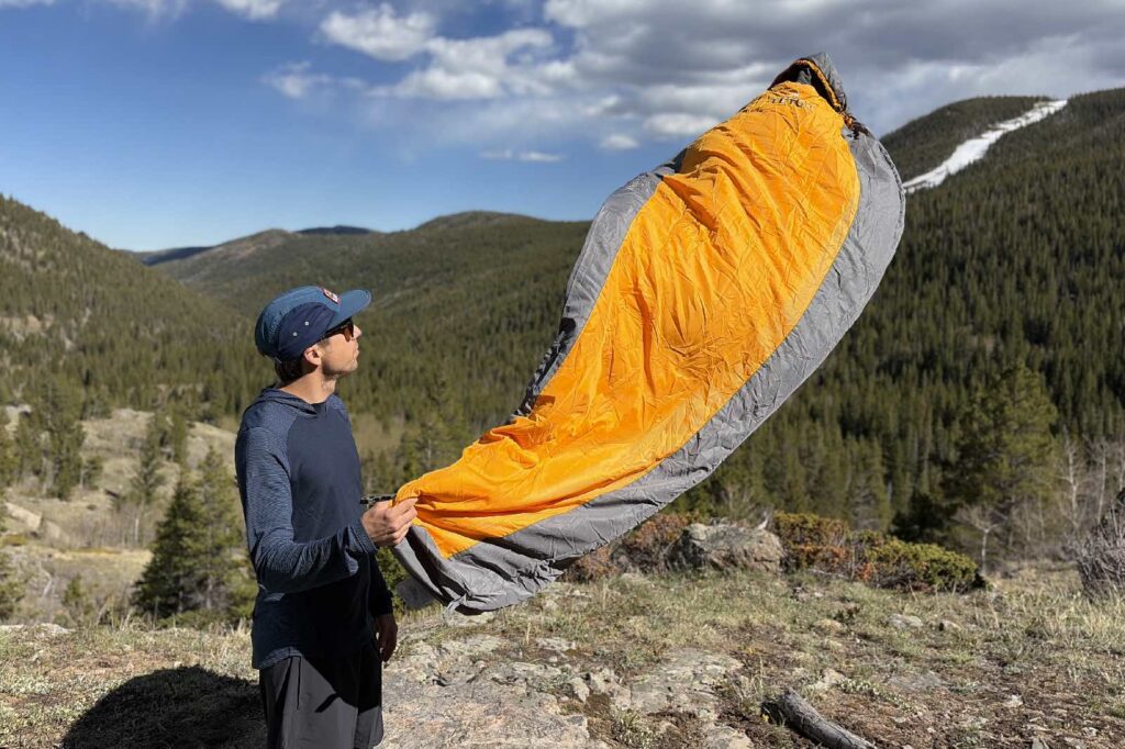 a hiker holds an orange and grey sleeping bag