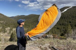 a hiker holds an orange and grey sleeping bag