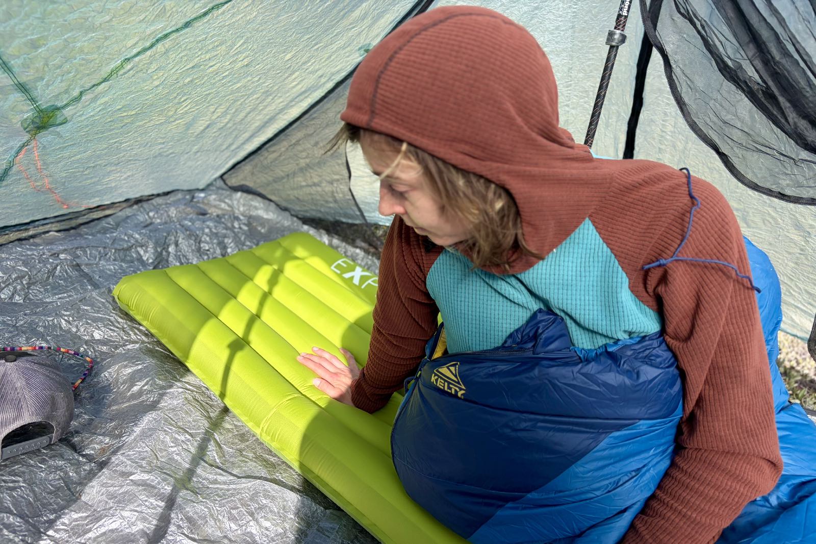 a hiker sits up and puts her hand on a green inflatable sleeping pad