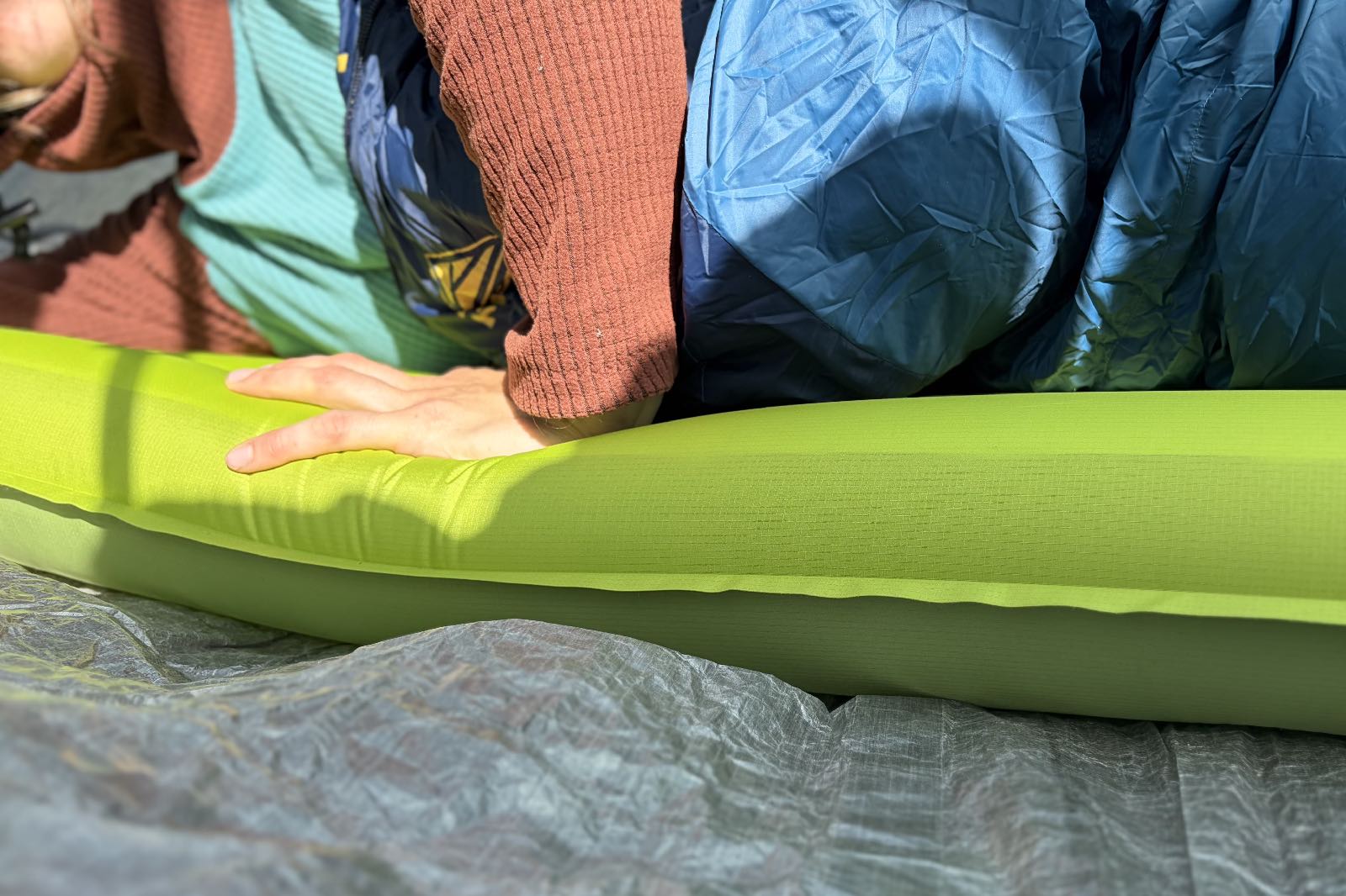 a hiker lays on a pushes her hand down onto a green inflatable sleeping pad