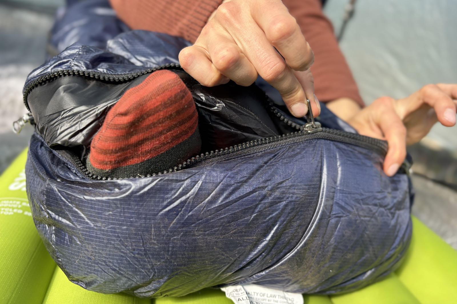 a close up of a hiker zipping the footbox of a sleeping bag closed